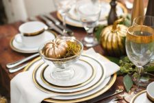a refined Thanksgiving tablescape with gold rimmer plates and glasses plus gilded pumpkins is cool