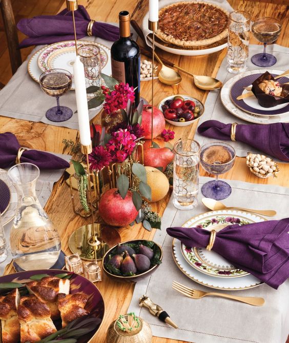 a refined Thanksgiving tablescape with neutral placemats, purple napkins, bold fuchsia blooms, gold touches and berries