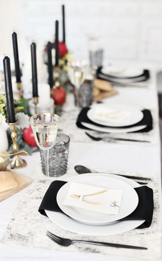 a refined Thanksgiving tablescape with white plates, black napkins and candles, pomegranates, greenery and black glasses