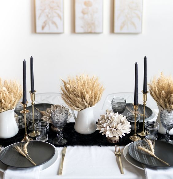 a refined modern Thanksgiving tablescape with a black runner, black plates, black candles, wheat in jugs and some dried blooms