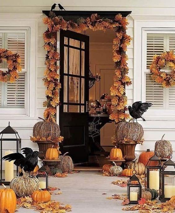 a rustic Halloween porch with fall leaves, faux and vine pumpkins, candle lanterns and blackbirds is very cool