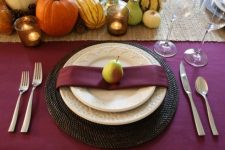 a rustic Thanksgiving table setting with a purple tablecloth and napkins, gourds, pumpkins, pears, candles and woven placemats