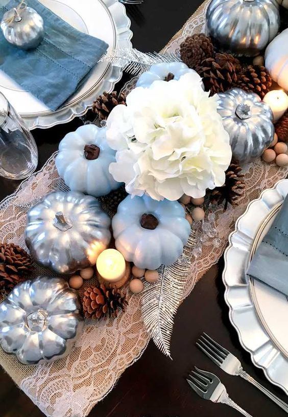 a rustic coastal Thanksgiving table with a lace runner, blue and silver pumpkins, white hydrangeas, pinecones and beads plus blue napkins