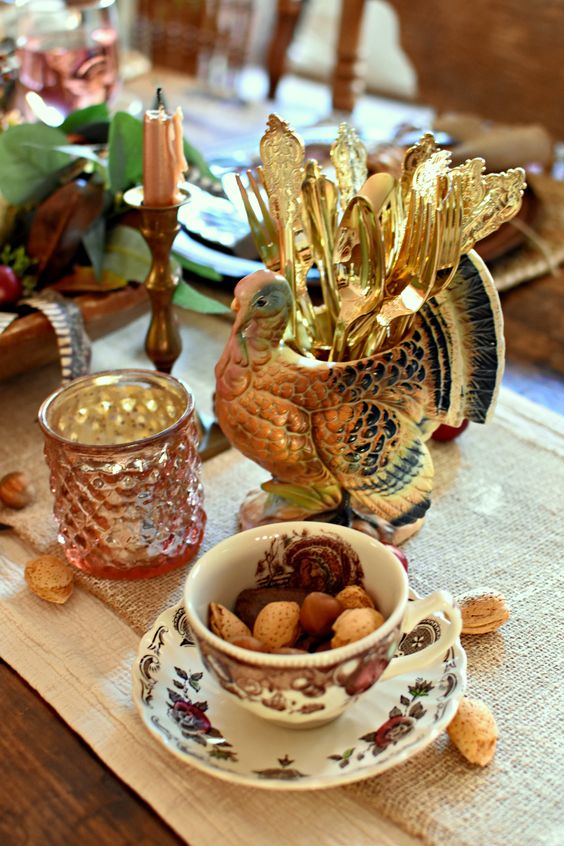 a rustic vintage Thanksgiving table with burlap runners, a turkey cutlery stand, floral porcelain and greenery