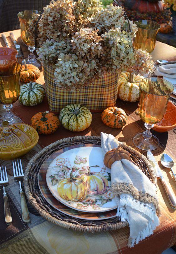 a rustic vintage Thanksgiving table with woven chargers, printed plates, natural pumpkins, a plaid box with hydrangeas