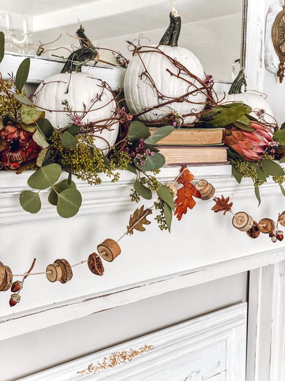 a rustic vintage mantel with greenery, pink blooms, white pumpkins and a garland with wood slices and nuts