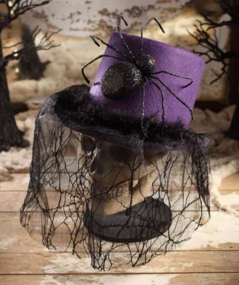a skull dressed into a purple hat with a large spider and a lace spiderweb veil is a creative old-fashioned decoration for Halloween