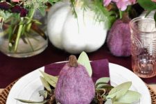 a stylish Thanksgiving tablescape with a purple table runner and napkins, purple felt pumpkins, white ones, peachy and pink blooms and greenery