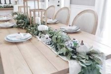 a table runner of greenery, white and plaid pumpkins and with candle lanterns is ideal for Thanksgiving