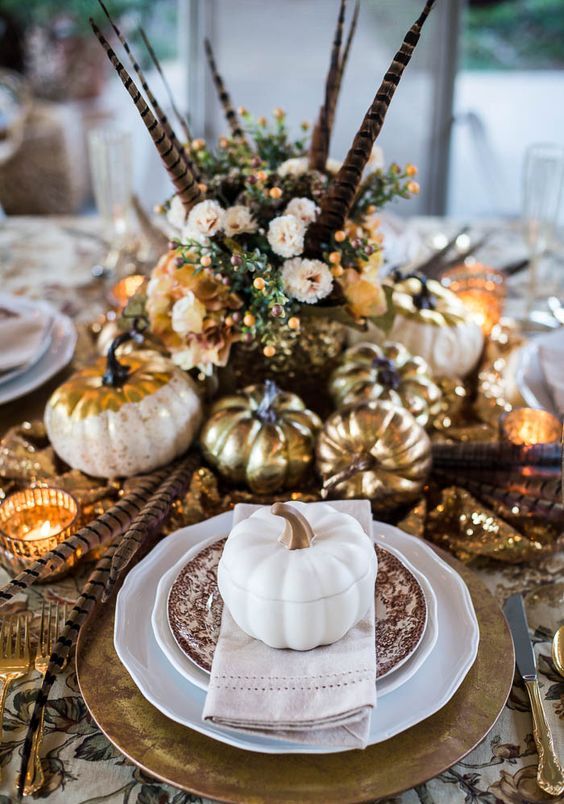 a vintage boho Thanksgiving tablescape with printed linens and plates, gold chargers, cutlery, pumpkins and candleholders, feathers and blush blooms