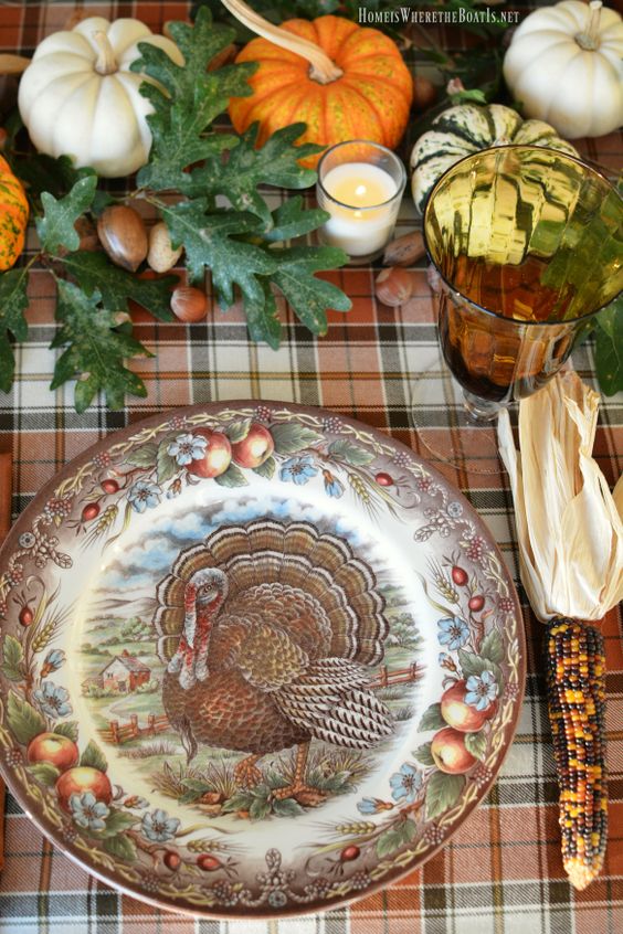a vintage rustic Thanksgiving table with a plaid tablecloth, a printed plate, leaves, acorns, pumpkins and candles