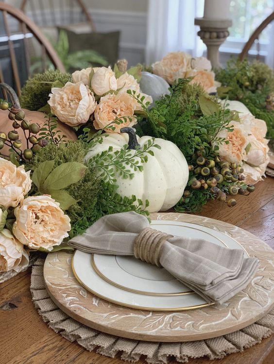 a vintage rustic Thanksgiving table with wooden chargers, burlap placemats, faux greenery, berries, peachy blooms and pumpkins