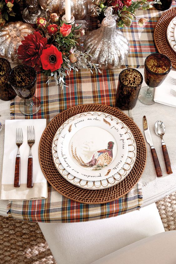 a vintage rustic Thanksgiving tablescape with a plaid runner, woven chargers, printed plates, vintage cutlery and bold blooms and glasses