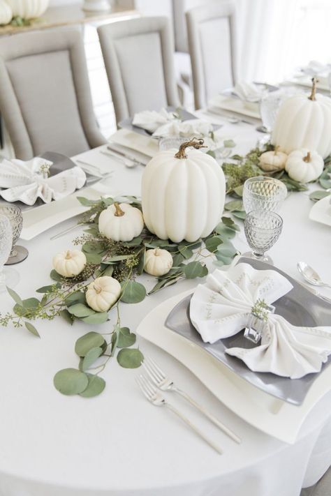 a white and neutral Thanksgiving tablescape with large and small pumpkins, eucalyptus, quirky plates and silver cutlery