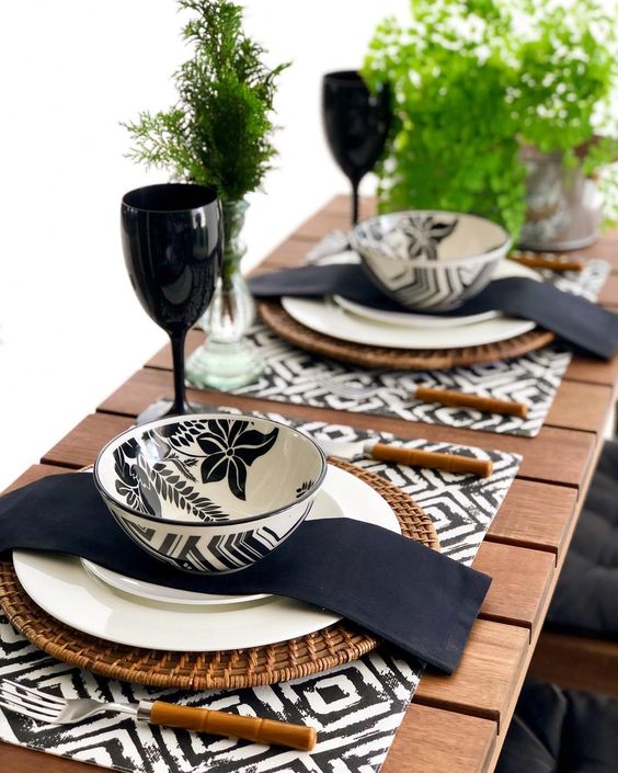 an eye-catchy black and white Thanksgiving tablescape with printed placemats, printed bowls, black napkins, greenery and black glasses