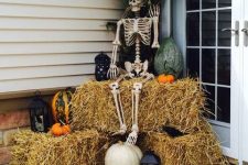 rustic Halloween decor with hay, bat candles, natural pumpkins, a skeleton and some husks plus a burlap bunting