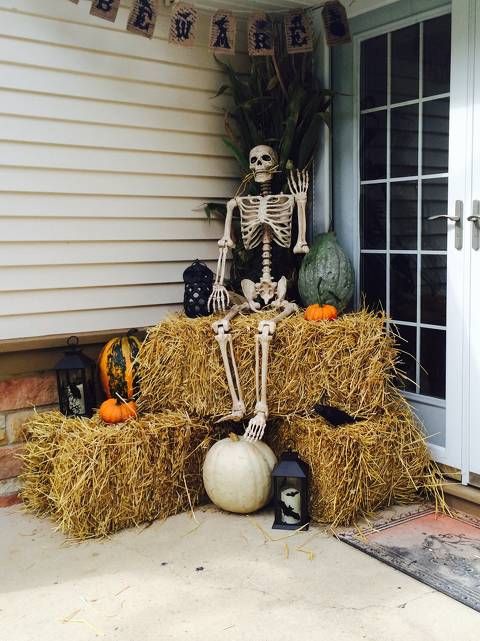 rustic Halloween decor with hay, bat candles, natural pumpkins, a skeleton and some husks plus a burlap bunting