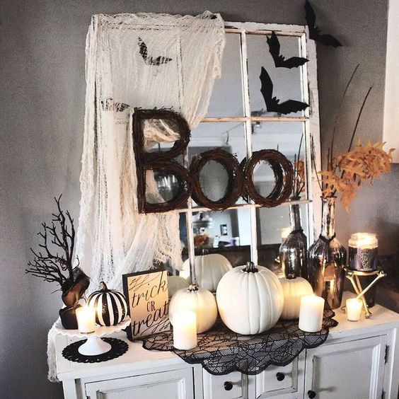 vintage Halloween decor in black and white, with a vintage mirror, some spiderweb, white pumpkins and candles, leaves and branches