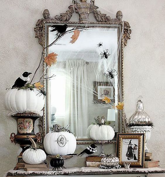 vintage Halloween decor with a large mirror in an ornated frame, white pumpkins with patterns and blackbirds plus spiders and fall leaves