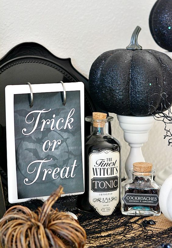 vintage Halloween decor with a sign, vintage potion bottles, white stands with black glitter pumpkins is a chic and bold idea