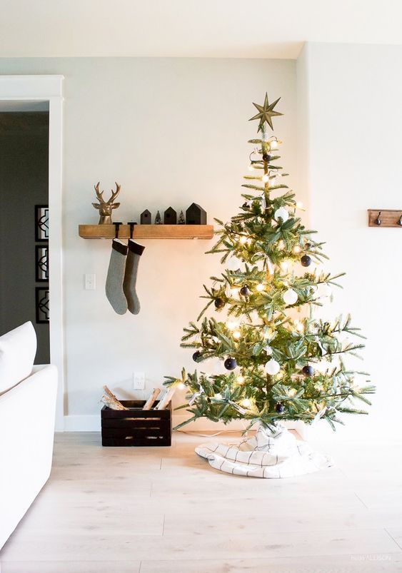 a Christmas tree with lights and black and white ornaments, black houses and stockings on the mantel and a crate with firewood