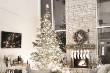 a Christmas tree with lights and white ornaments, white stockings, a fir garland and a fir wreath with red berries and mini trees
