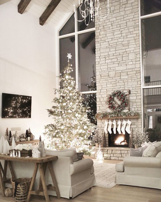 a Christmas tree with lights and white ornaments, white stockings, a fir garland and a fir wreath with red berries and mini trees