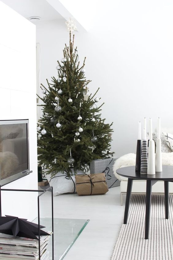 a Christmas tree with silver and clear ornaments and an arrangement of black and white candleholders for a Nordic feel