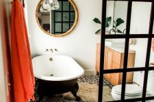 a beautiful eclectic bathroom with white walls, black and white Moroccan tiles, a black clawfoot tub, a neutral vanity, a black glass shower wall, a bold pompom bench