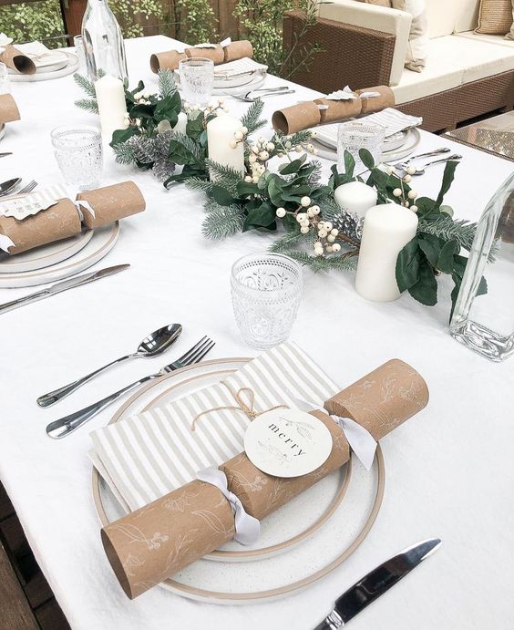 a beautiful neutral Christmas tablescape with a white tablecloth and napkins, white porcelain, an evergreen runner and white berries