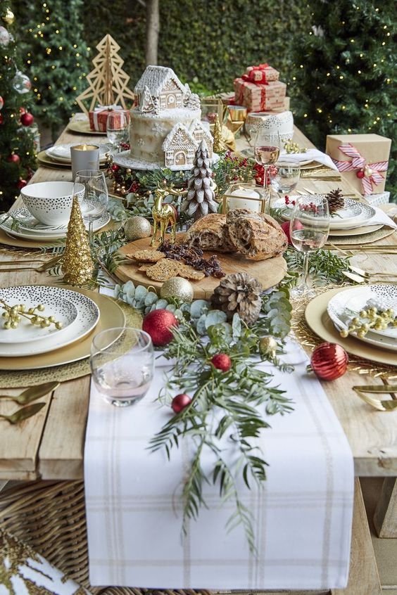 a beautiful outdoor Christmas tablescape with a neutral runner, a board with food and deer, tabletop Christmas trees and pinecones
