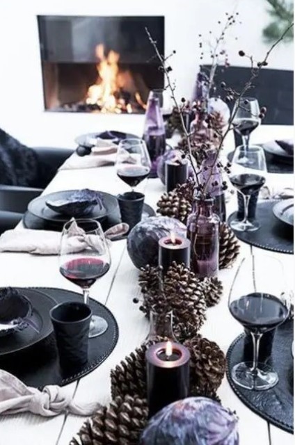 a black and purple New Year's table setting with oversized pinecones, purple candles and black chargers and plates