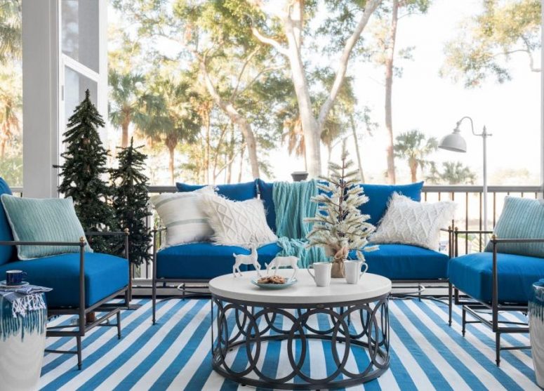 a blue and white coastal Christmas terrace with blue furniture, neutral pillows, Christmas trees, deer and a striped rug