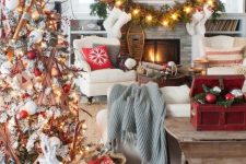 a bold and creative Christmas living room with a white tree with red and white ornaments and skis, a fir garland with lights, red candleholders and a red box with ornaments
