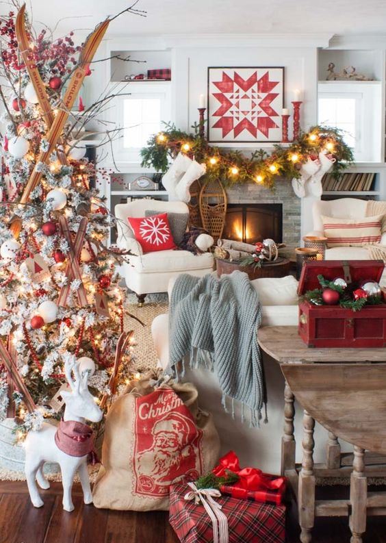 a bold and creative Christmas living room with a white tree with red and white ornaments and skis, a fir garland with lights, red candleholders and a red box with ornaments