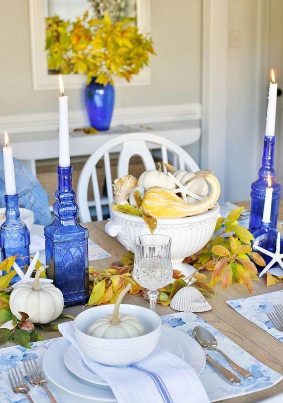 a bold blue and yellow Thanksgiving table setting with blue bottle candleholders and blue printed placemats and napkins