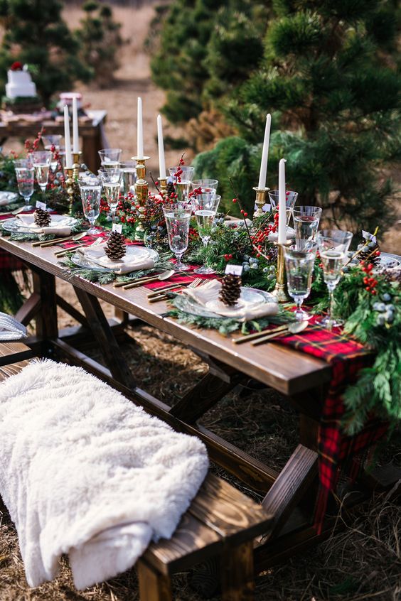 a bold outdoor Christmas tablescape with an evergreen and red plaid runner, evergreen placemats, tall and thin candles, berries on the table and some pinecones