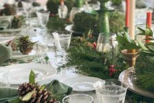 a bright Christmas tablescape with printed placemats, printed plates, an evergreen runner with berries, colored candles in green candleholders