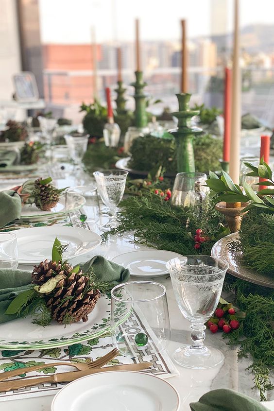 a bright Christmas tablescape with printed placemats, printed plates, an evergreen runner with berries, colored candles in green candleholders