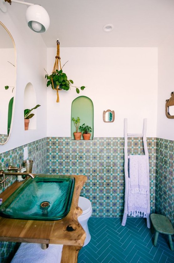 a bright bathroom with colorful Moroccan tiles and blue chevron tiles on the floor, a turquoise glass sink and potted plants
