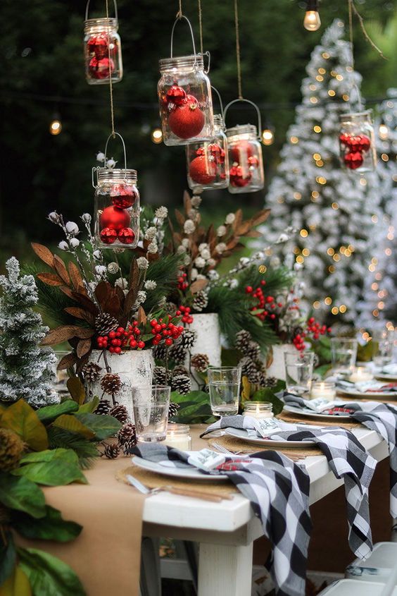 a bright outdoor Christmas tablescape with a paper runner and placemats, buffalo check napkins, bold evergreens, snowy pinecones and berries, red ornaments over the table