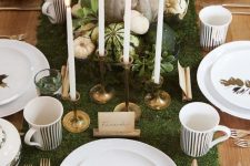 a chic Thanksgiving tablescape with a moss runner, pumpkins, greenery, candles and and gold leaves