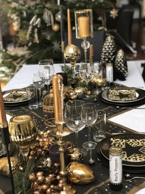 a chic black and gold NYE party tablescape with black table runners and placemats, black and gold plates, gold candles and candleholders