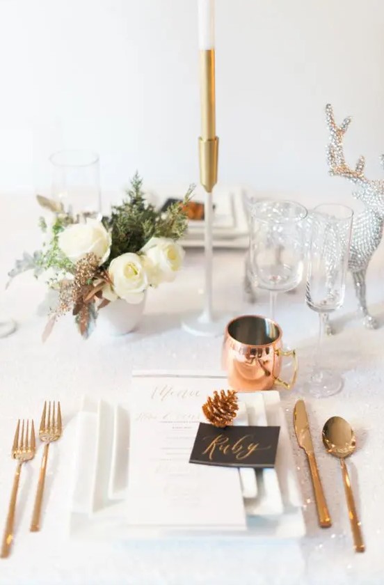 a chic holiday tablescape with white blooms, copper cutlery and mugs and a silver deer figurine for a sparkly touch