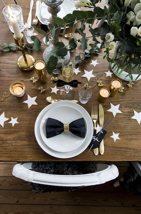 a chic table setting with white and gold stars, white blooms, eucalyptus, gold cutlery and candle holders