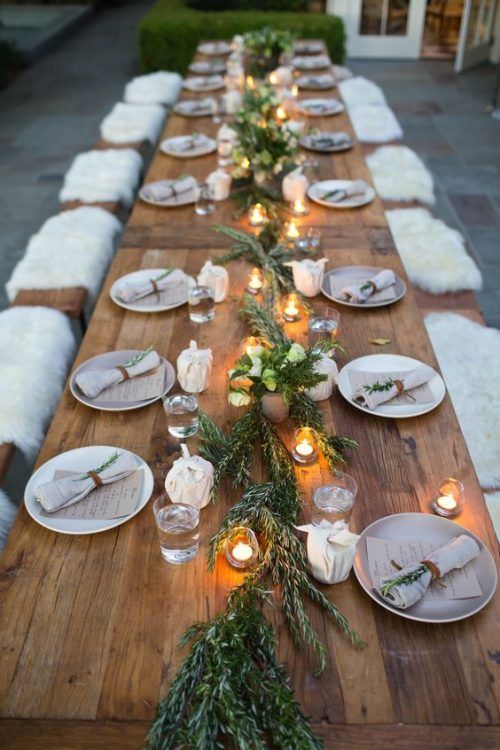a christmas party tablescape with neutral porcelain, an evergreen runner, candles and neutral napkins with greenery