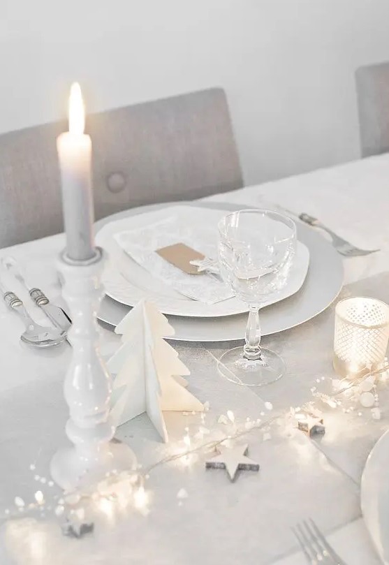 a clean white tablescape with a dove grey table runner, LEDs, stars, candles and wooden fir trees