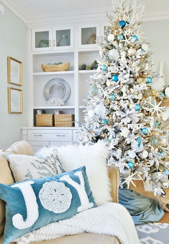 a coastal Christmas space with a flocked Christmas tree with mint, blue ornaments, starfish, lights and corals and a duo of lovely beach-inspired pillows