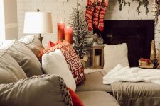 a cozy Christmas living room with fir branches, berries, antlers and red stockings on the mantel, red candles and printed pillows