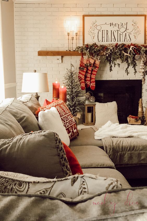 a cozy Christmas living room with fir branches, berries, antlers and red stockings on the mantel, red candles and printed pillows